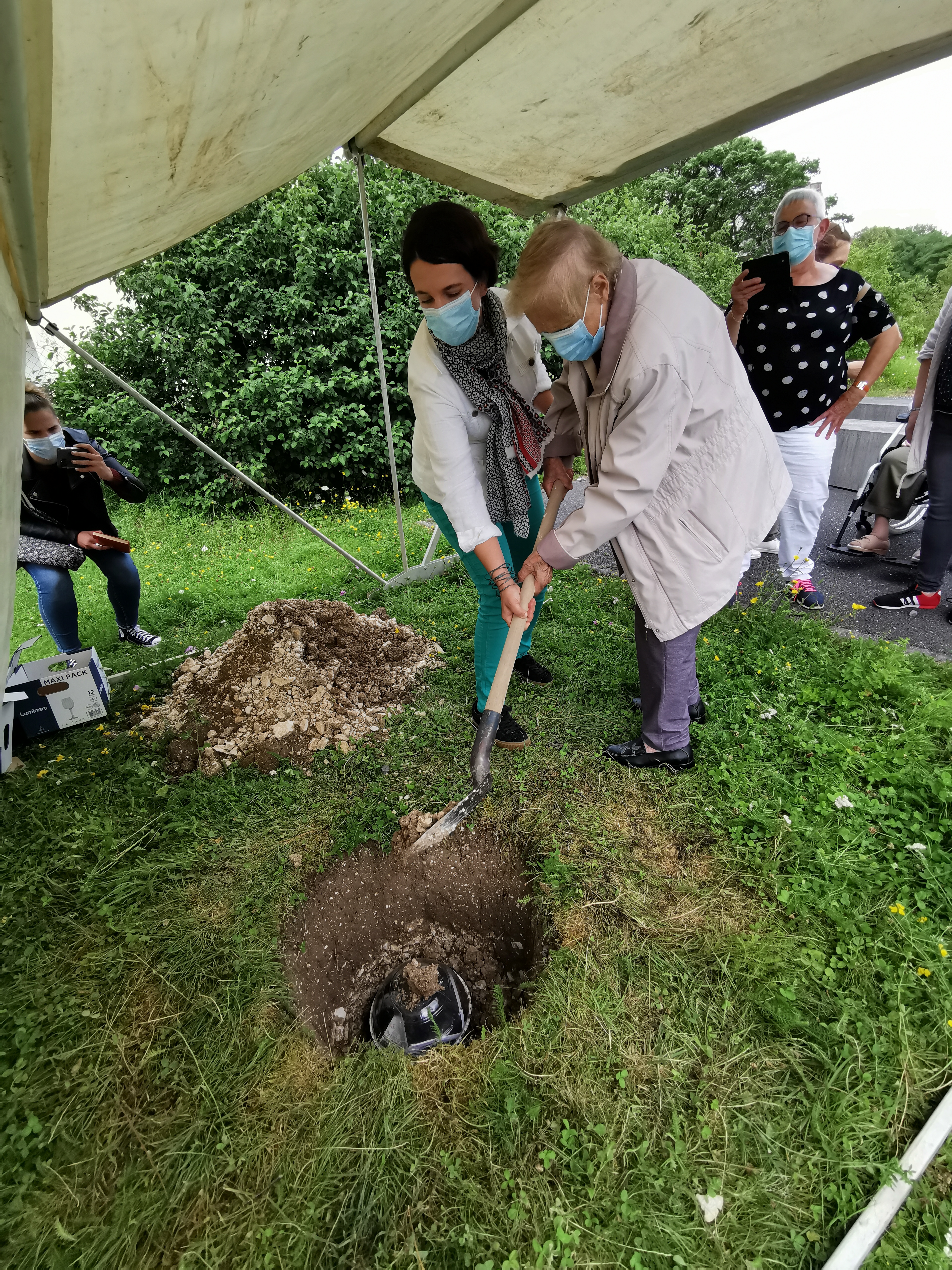 Julie Lamart Lule, responsable de la médiation à la maison de l'Archéologie et une résidente d'un Ehpad ensevelissent ensemble la capsule avec l'aide d'une pelle