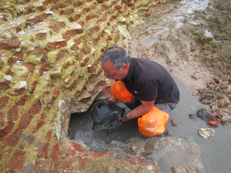 Photo d'un archéologue retirant un casque du canal du batardeau.