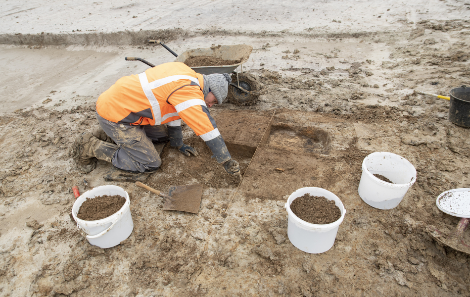 Photo d’un archéologue prélevant des sédiments du sol. Des seaux servent à recueillir ces sédiments.