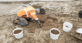 Photo d’un archéologue prélevant des sédiments du sol. Des seaux servent à recueillir ces sédiments.